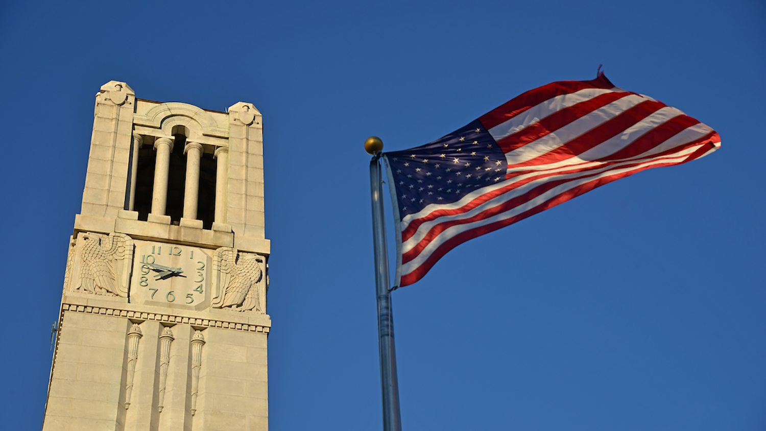 Early morning sun cuts across the Memorial Belltower and the American flag.