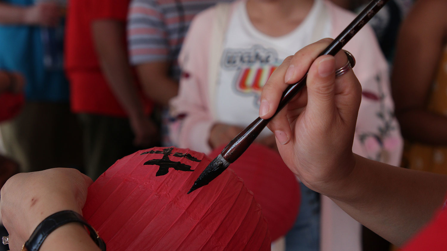 A person painting calligraphy on a Chinese lantern