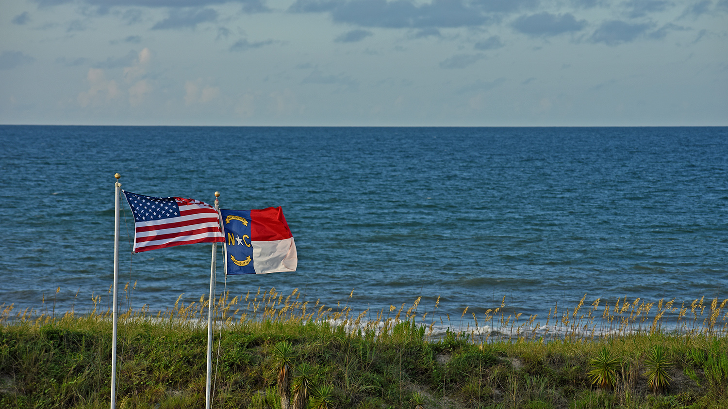US and NC flags flap in the summer breeze along the dunes of Atlantic Beach.