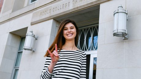 Sarah Daw making the Wolfpack hand sign in front of the Poole College of Management.