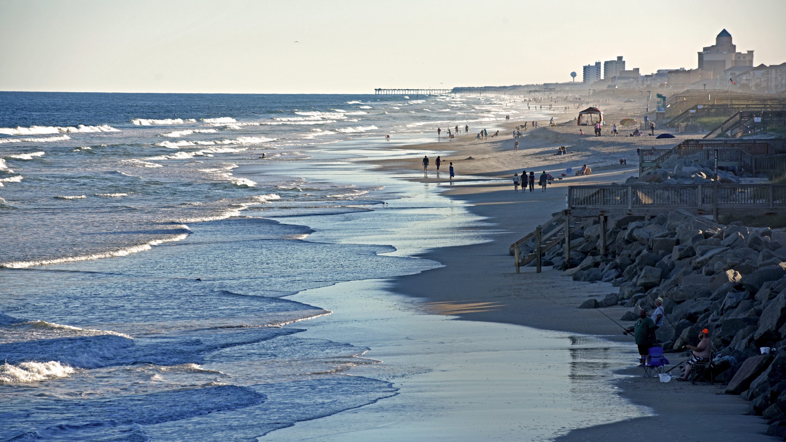 Atlantic Ocean waves rush the shore at Carolina Beach as beachgoers walk the surf near sunset.
