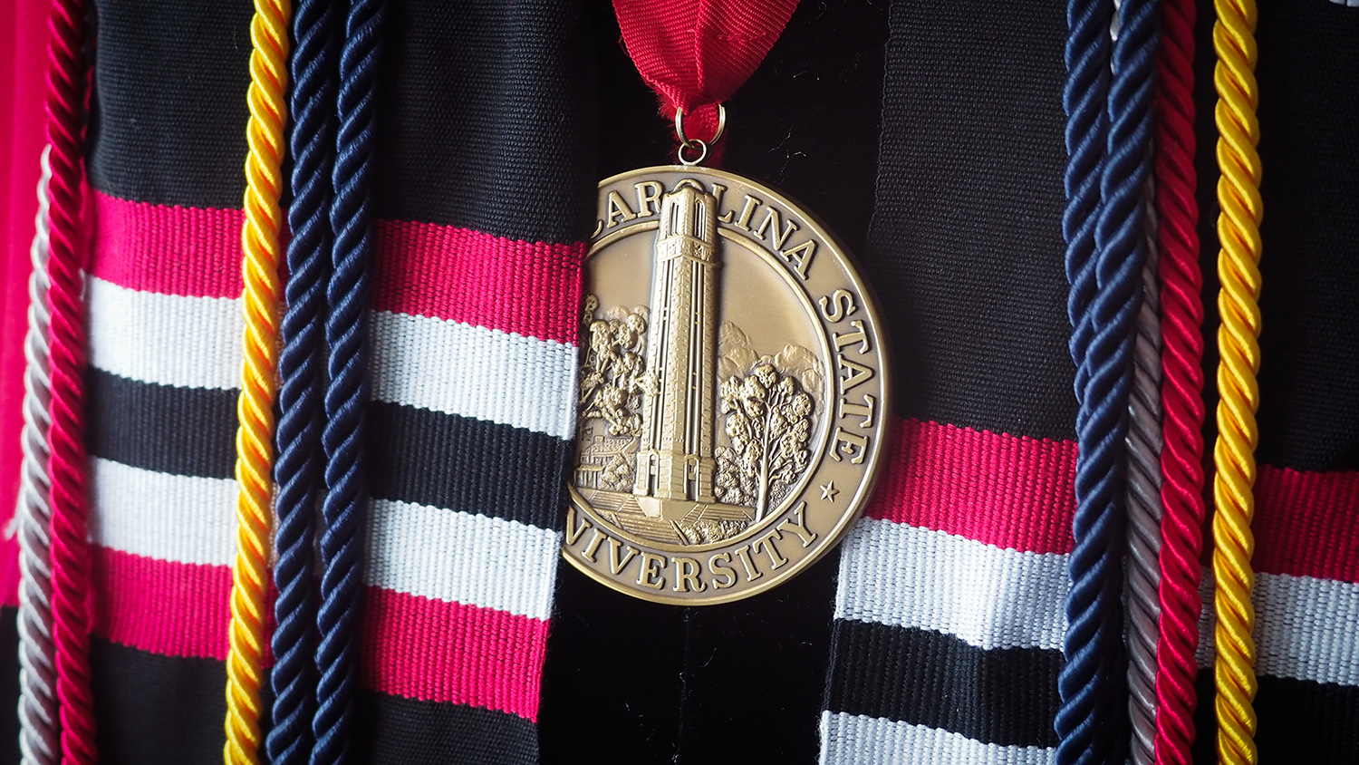 An NC State medallion hangs on an NC State graduate at Carter Finley stadium.