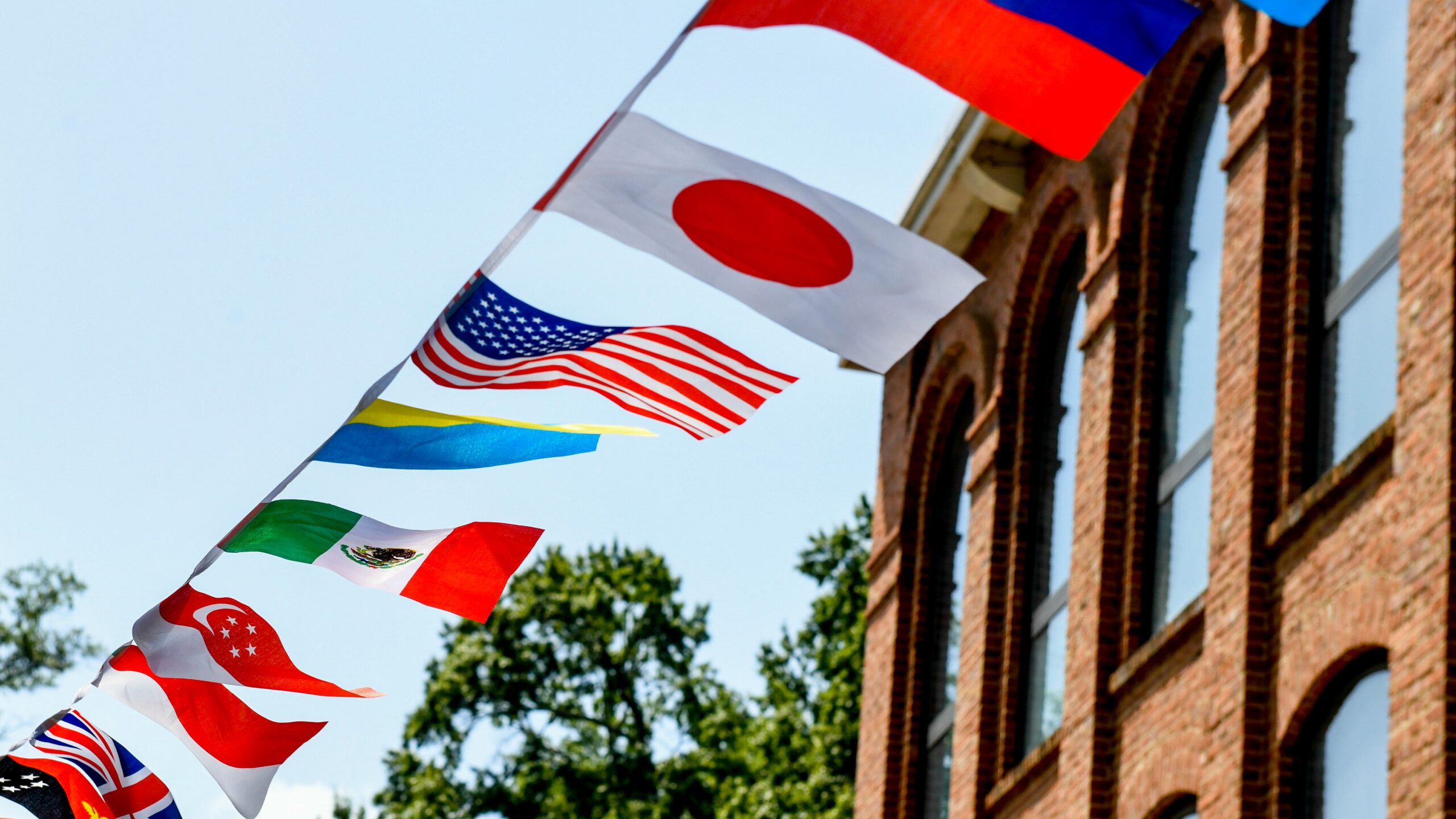 String of international flags against a blue sky next to a brick building