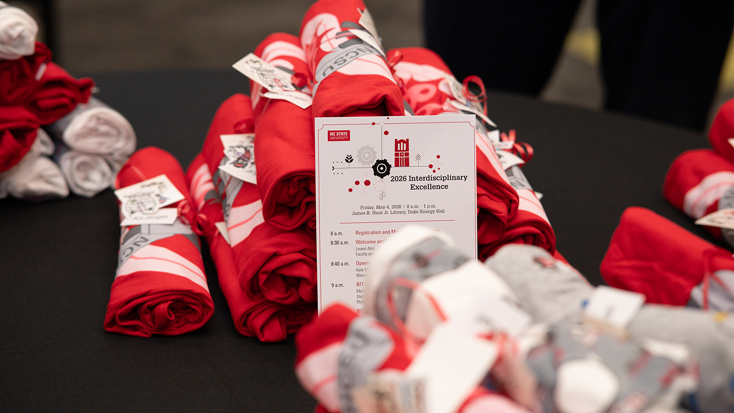 The Interdisciplinary Excellence Celebration event itinerary sits on a table with t-shirts being handed out by the BIT Program.